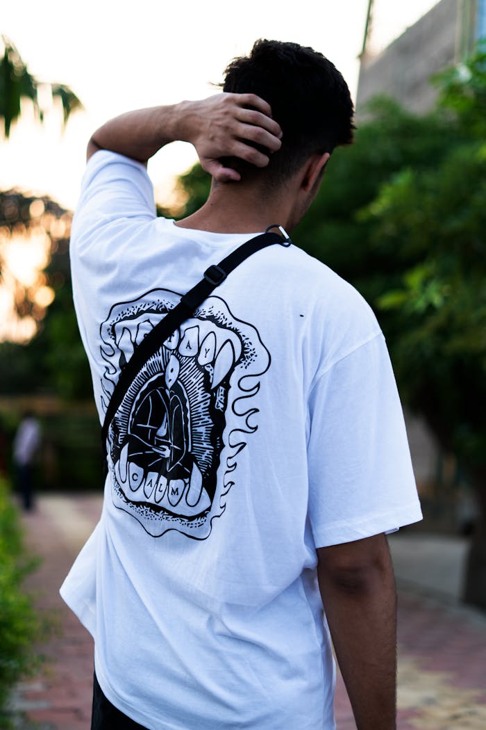 Man in streetwear poses outdoors with hand on head, showing unique shirt design.